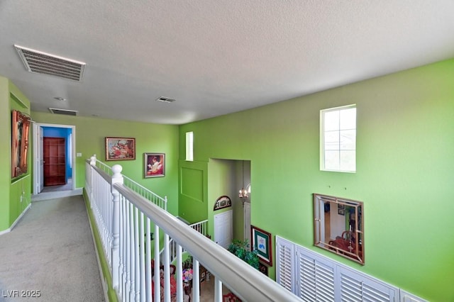 corridor featuring carpet, visible vents, a textured ceiling, and an upstairs landing