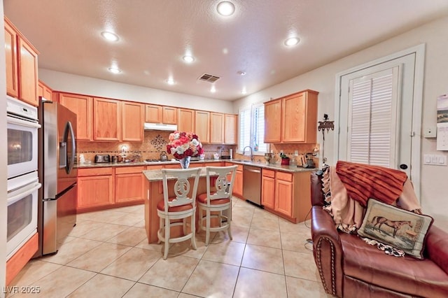 kitchen featuring light tile patterned floors, visible vents, appliances with stainless steel finishes, a center island, and a sink