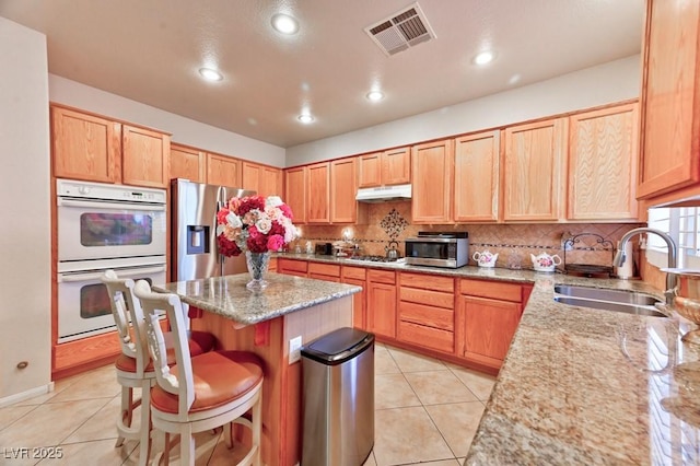 kitchen with stainless steel appliances, tasteful backsplash, visible vents, a sink, and under cabinet range hood