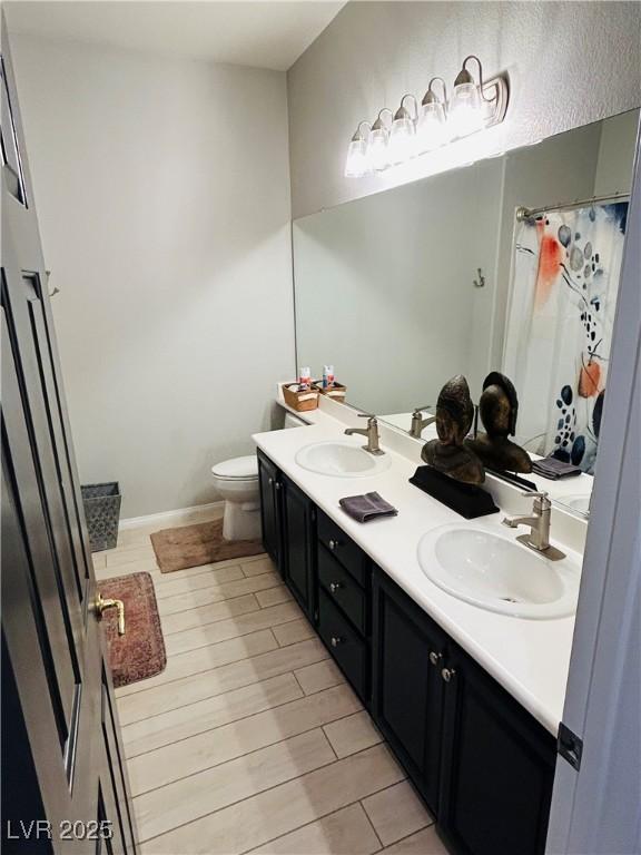 full bath with double vanity, a sink, toilet, and wood tiled floor