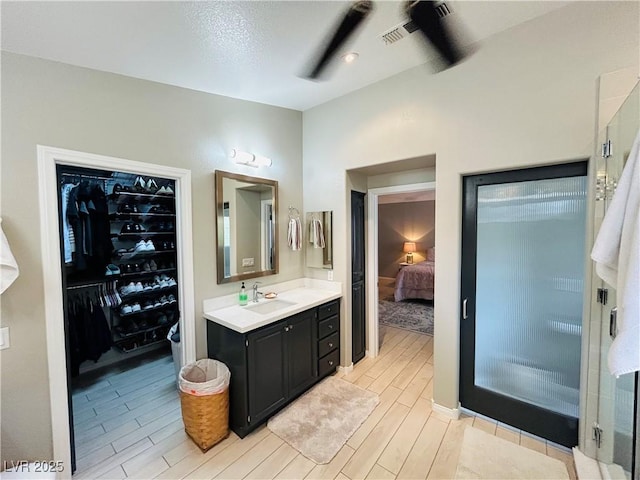 ensuite bathroom with ensuite bathroom, wood finish floors, vanity, a stall shower, and a walk in closet