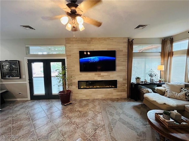 living room featuring ceiling fan, a fireplace, visible vents, and french doors