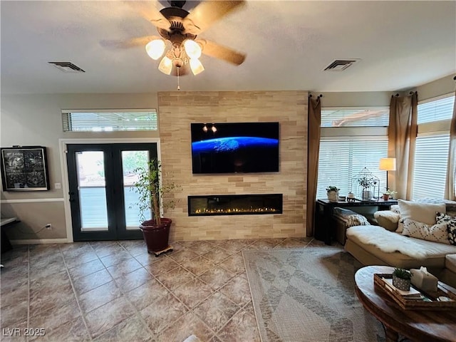 living area featuring baseboards, a ceiling fan, a large fireplace, and visible vents