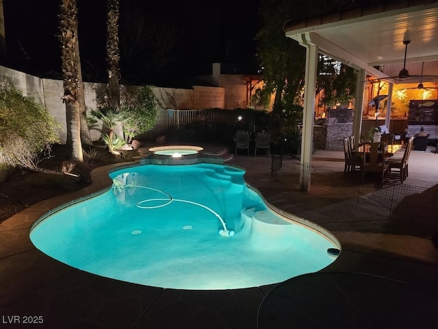 pool at night featuring a patio, a ceiling fan, fence, and a pool with connected hot tub