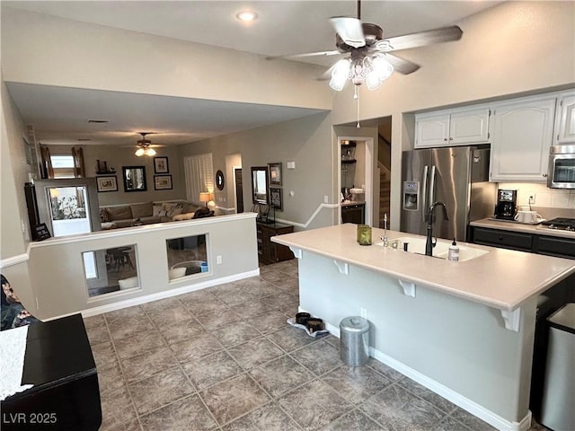 kitchen featuring a breakfast bar area, stainless steel appliances, light countertops, open floor plan, and a sink