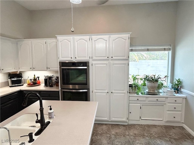 kitchen featuring double oven, white cabinetry, light countertops, and a sink