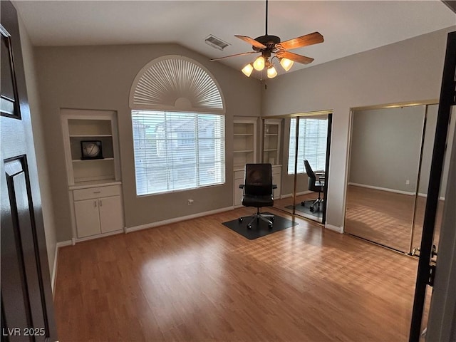 office featuring visible vents, a ceiling fan, built in shelves, and wood finished floors