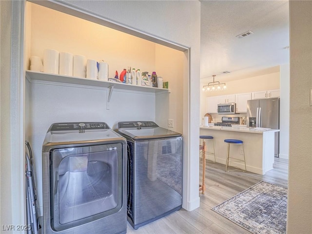 washroom featuring a textured ceiling, laundry area, separate washer and dryer, visible vents, and light wood-style floors