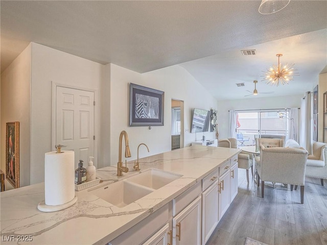 kitchen featuring light stone counters, light wood-style flooring, a sink, white cabinetry, and open floor plan