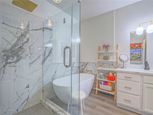 bathroom with a freestanding bath, vanity, a marble finish shower, and wood finished floors