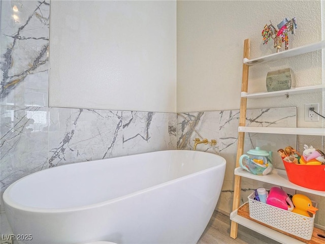 bathroom featuring wood finished floors, a freestanding tub, and tile walls