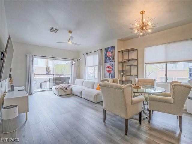 living room with visible vents, wood finished floors, and ceiling fan with notable chandelier