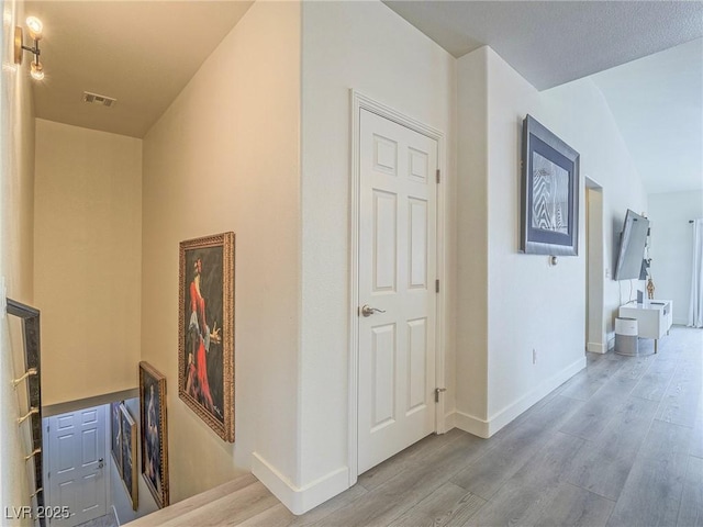 corridor with an upstairs landing, wood finished floors, visible vents, and baseboards