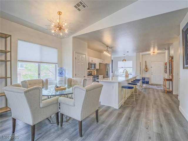 dining space featuring an inviting chandelier, baseboards, visible vents, and light wood-style floors