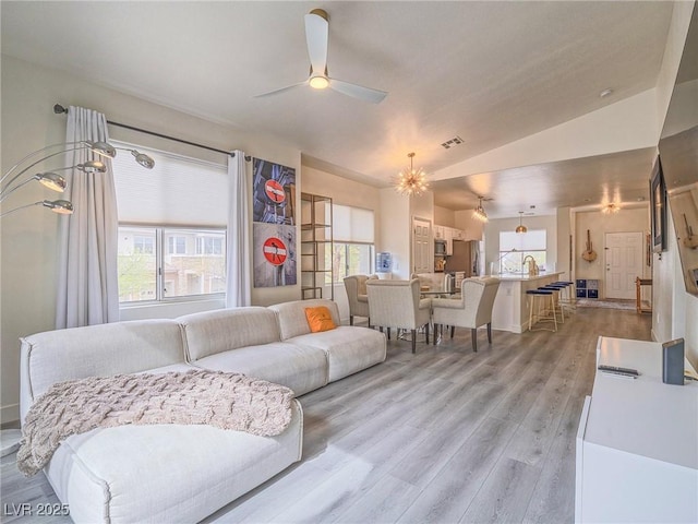 living room with light wood-style floors, a healthy amount of sunlight, visible vents, and vaulted ceiling