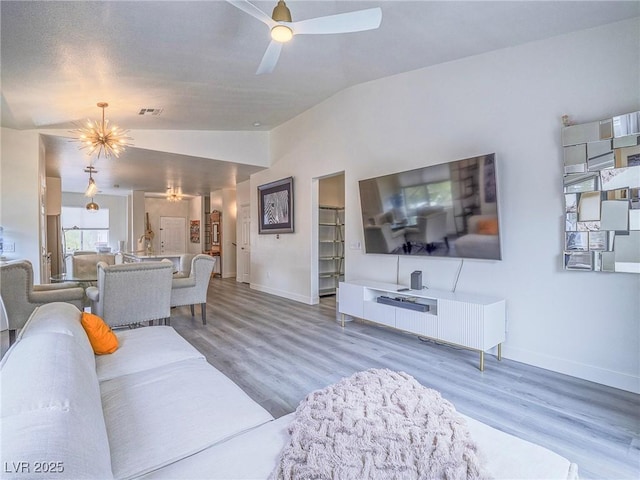 living area with vaulted ceiling, ceiling fan with notable chandelier, wood finished floors, and baseboards