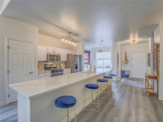 kitchen featuring appliances with stainless steel finishes, a breakfast bar, wood finished floors, light stone countertops, and a sink