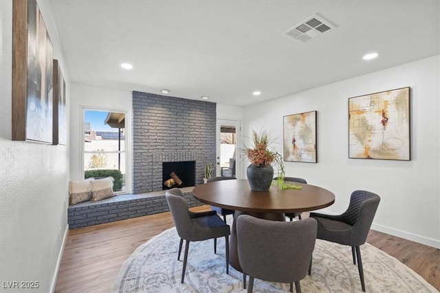 dining room with baseboards, visible vents, wood finished floors, a brick fireplace, and recessed lighting