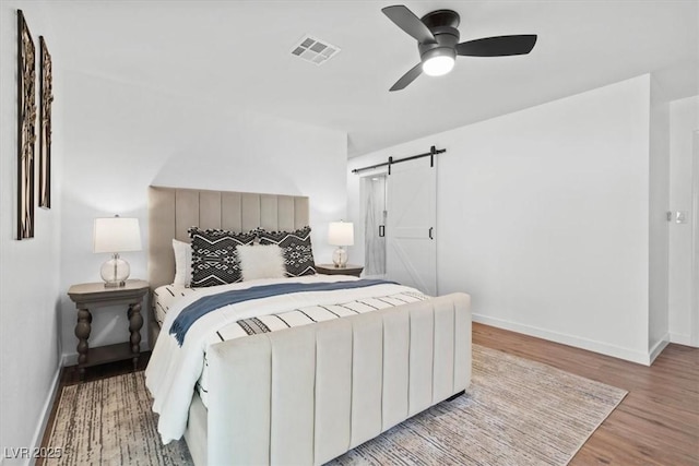 bedroom with visible vents, a barn door, ceiling fan, wood finished floors, and baseboards