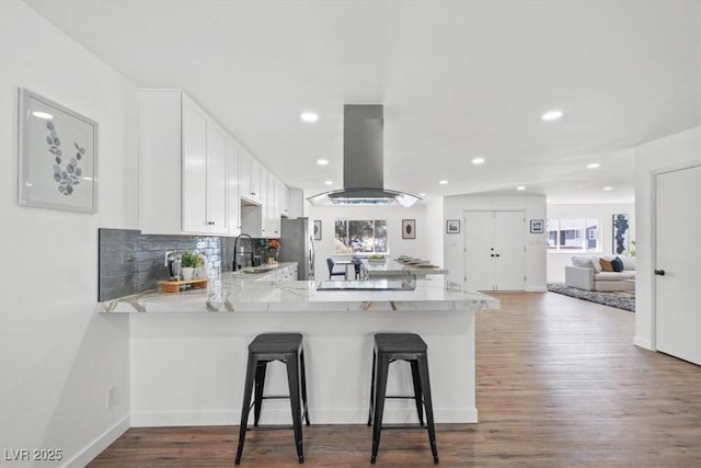 kitchen with island range hood, white cabinets, dark wood-type flooring, a peninsula, and a sink