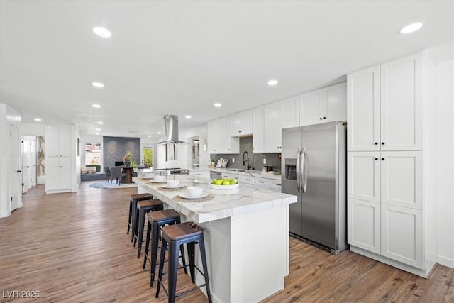 kitchen with a center island, stainless steel refrigerator with ice dispenser, white cabinetry, a sink, and ventilation hood