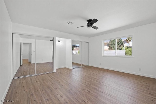 unfurnished bedroom with multiple closets, visible vents, baseboards, and wood finished floors