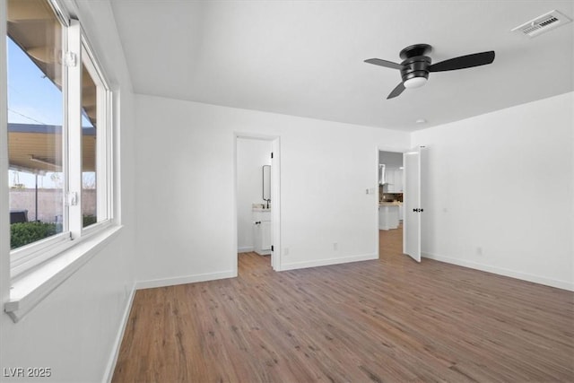 empty room with a ceiling fan, wood finished floors, visible vents, and baseboards