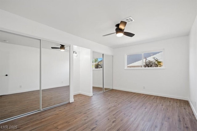 unfurnished bedroom with baseboards, visible vents, a ceiling fan, wood finished floors, and two closets