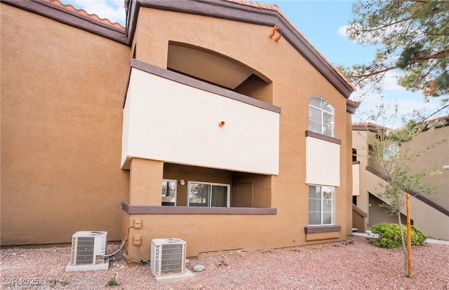 rear view of house with stucco siding, ac unit, and a tiled roof