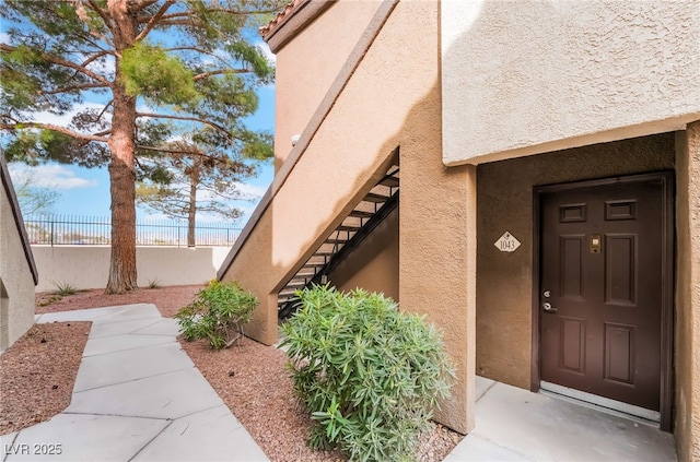 entrance to property featuring fence and stucco siding