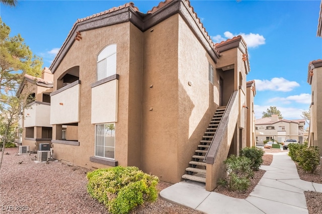 view of side of property with a tile roof, stairs, central AC, and stucco siding