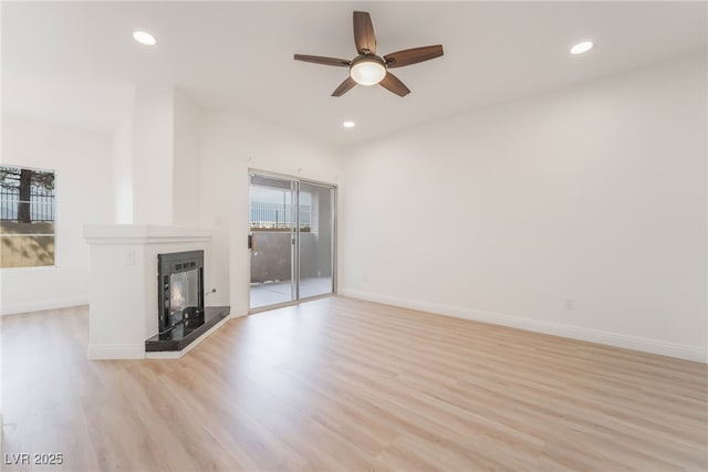 unfurnished living room featuring light wood-style floors, recessed lighting, a fireplace with raised hearth, and baseboards