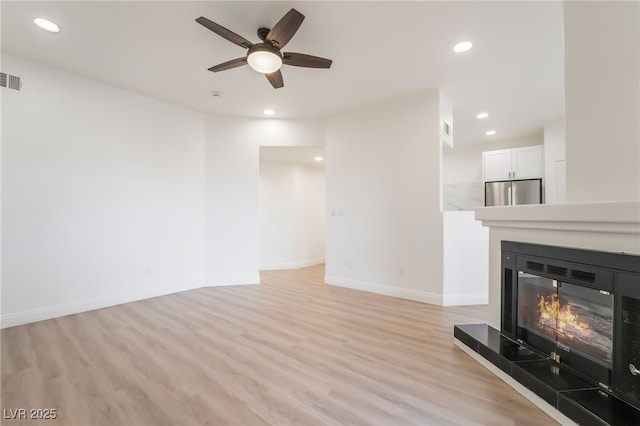 unfurnished living room featuring light wood-type flooring, a glass covered fireplace, baseboards, and recessed lighting