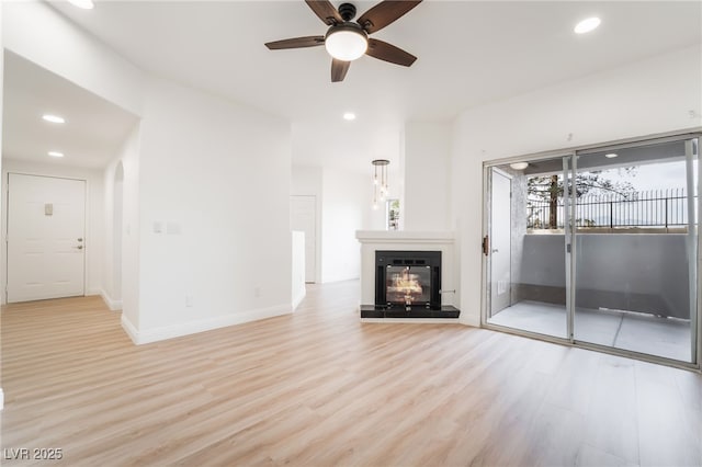 unfurnished living room featuring light wood-style floors, a glass covered fireplace, baseboards, and recessed lighting