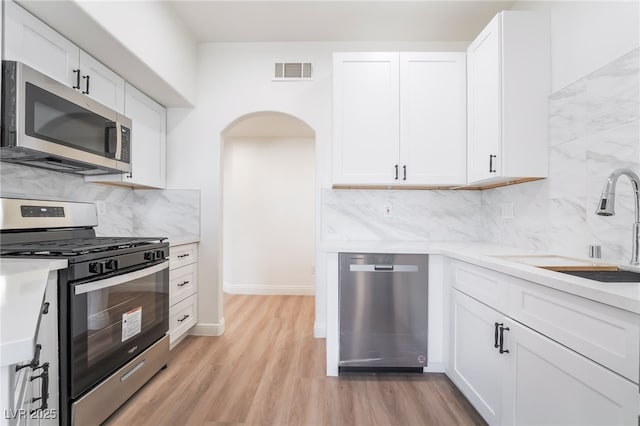 kitchen featuring light wood finished floors, visible vents, arched walkways, appliances with stainless steel finishes, and a sink