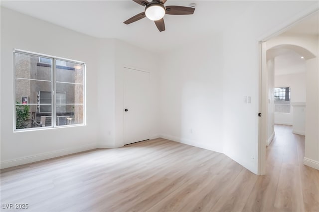 spare room with arched walkways, light wood-type flooring, a ceiling fan, and baseboards