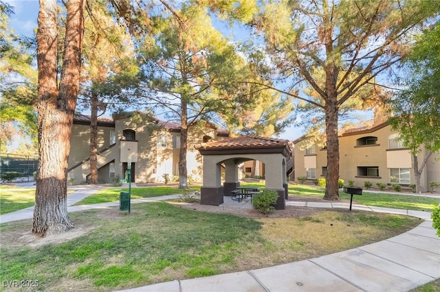 view of front of home featuring a front yard, a tile roof, a gazebo, and stucco siding