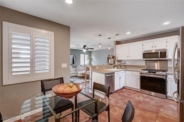 kitchen featuring a peninsula, a sink, decorative backsplash, appliances with stainless steel finishes, and white cabinetry