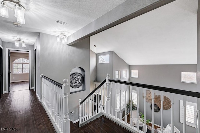 hallway with an upstairs landing, visible vents, wood-type flooring, and a textured ceiling