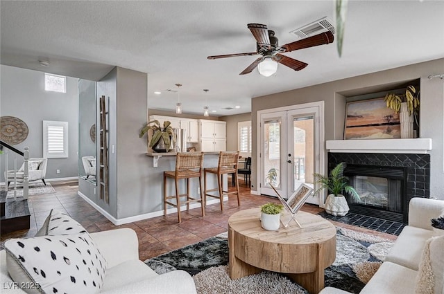 tiled living room with a wealth of natural light, visible vents, a fireplace, and french doors