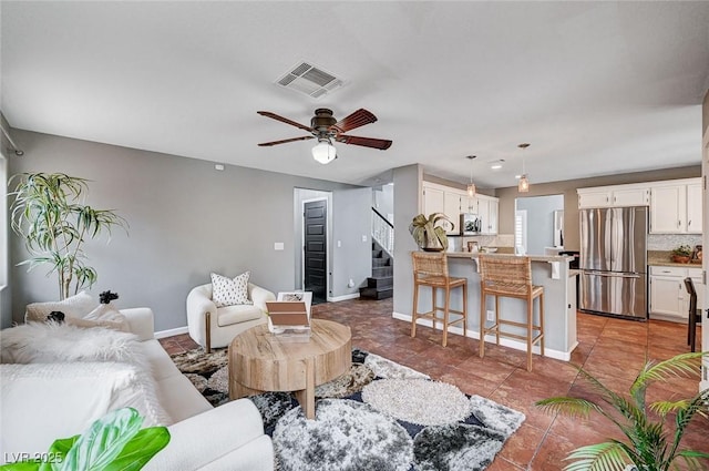 living area with stairway, baseboards, visible vents, and ceiling fan