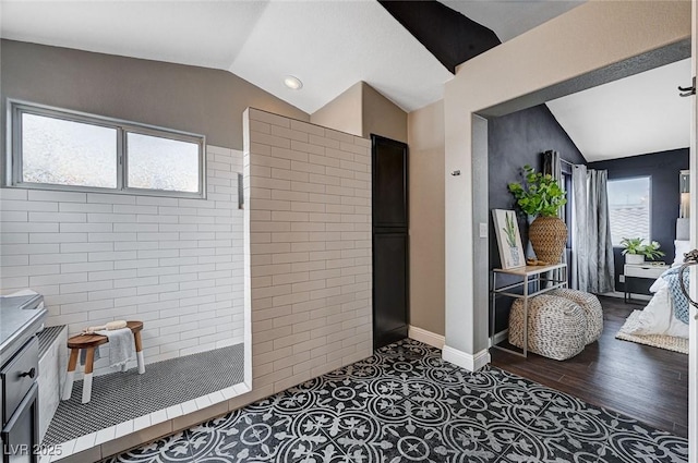 interior space with lofted ceiling, a walk in shower, wood finished floors, ensuite bath, and baseboards