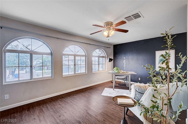 living area featuring a ceiling fan, wood finished floors, visible vents, and baseboards