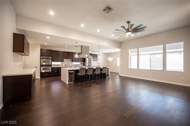 kitchen with stainless steel double oven, visible vents, dark brown cabinets, light countertops, and island exhaust hood