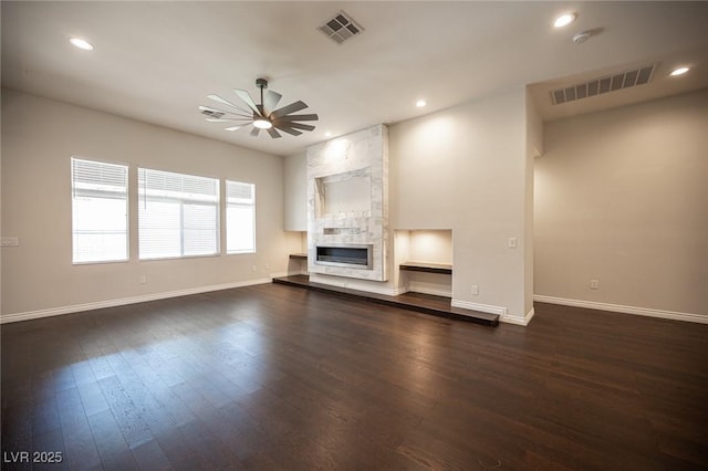 unfurnished living room with dark wood-type flooring, a large fireplace, visible vents, and ceiling fan