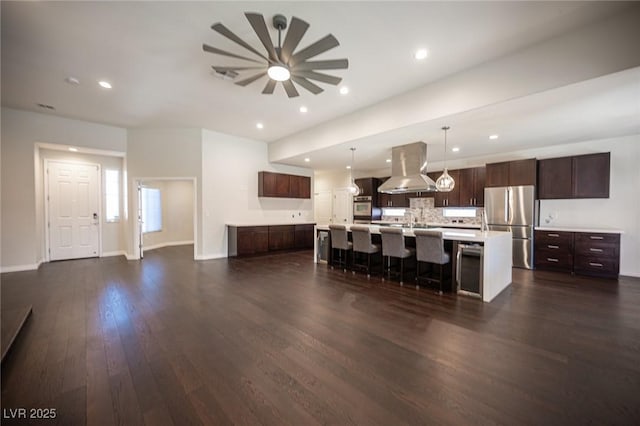 kitchen featuring dark brown cabinetry, island range hood, dark wood-type flooring, stainless steel appliances, and light countertops