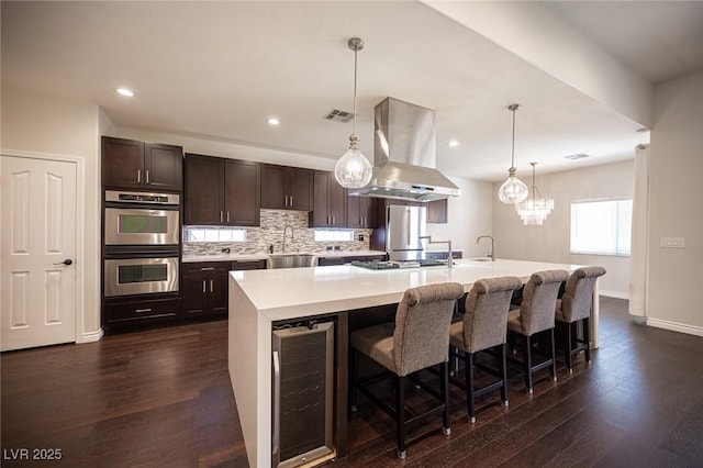 kitchen with beverage cooler, visible vents, appliances with stainless steel finishes, dark wood-style floors, and island exhaust hood