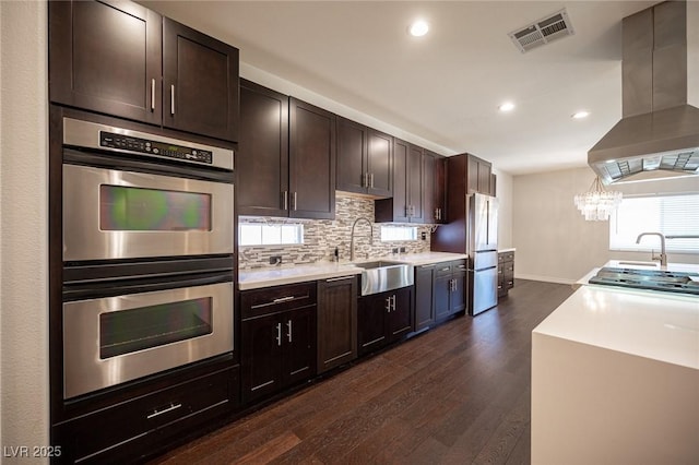 kitchen featuring stainless steel appliances, visible vents, backsplash, a sink, and island range hood