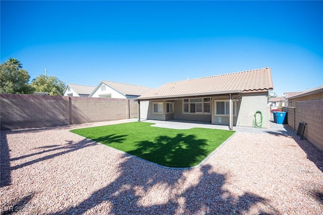 rear view of property with a fenced backyard, a tiled roof, a lawn, stucco siding, and a patio area