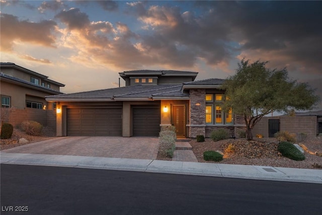 prairie-style house featuring a garage, stone siding, decorative driveway, and stucco siding